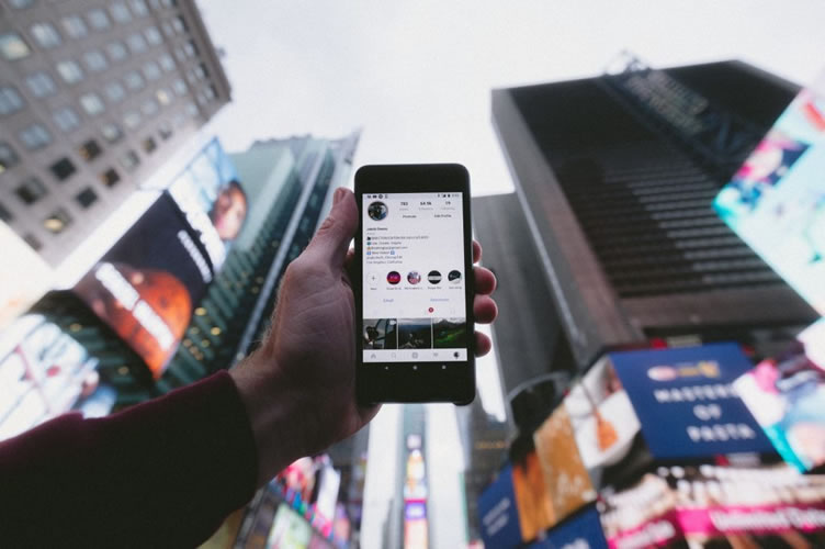 Corretor de imóveis com celular na mão em uma grande avenida com o aplicativo do Instagram Stories aberto. Para faze anúncios.