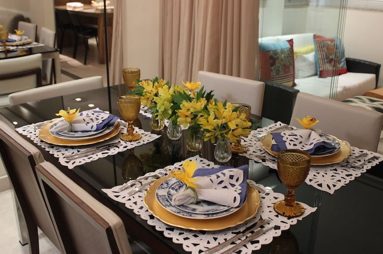 Mesa de jantar posta com arranjo de flores amarelas em cima. Pronta para uma excelente apresentação do imóvel.