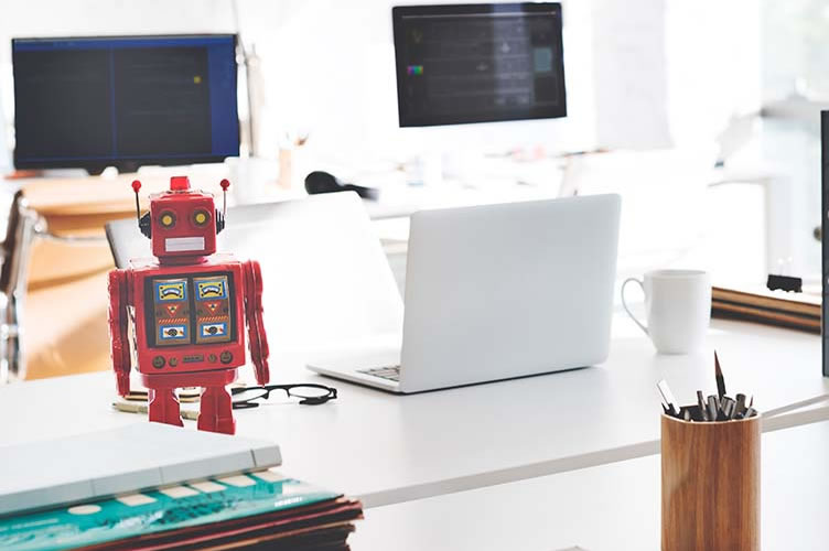 Um robô ao lado de um notebook branco na imobiliária. Para simbolizar a utilização de chatbot para automatizar o marketing imobiliário.