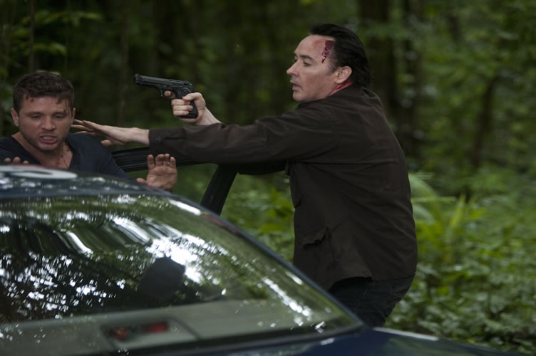 Cena de filme de ação, onde o ator aponta uma arma para o outro para ele executar algo. Apela a ação